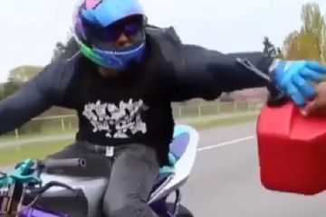 Pengendara motor mengisi bahan bakar saat motornya melaju kencang.